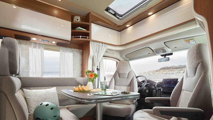 graue Sitzgruppe an gedecktem Tisch mit drehbaren Fahrer- und Beifahrersitzen mit Blick auf einen Strand 