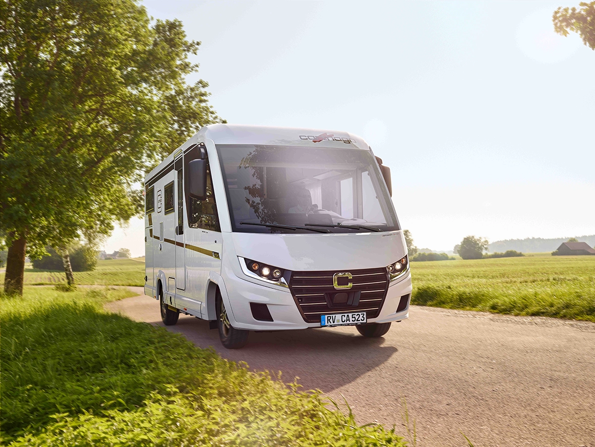 weißer, integrierter Carthago auf einer Landstraße mit Wiese und Bäumen bei Sonnenlicht