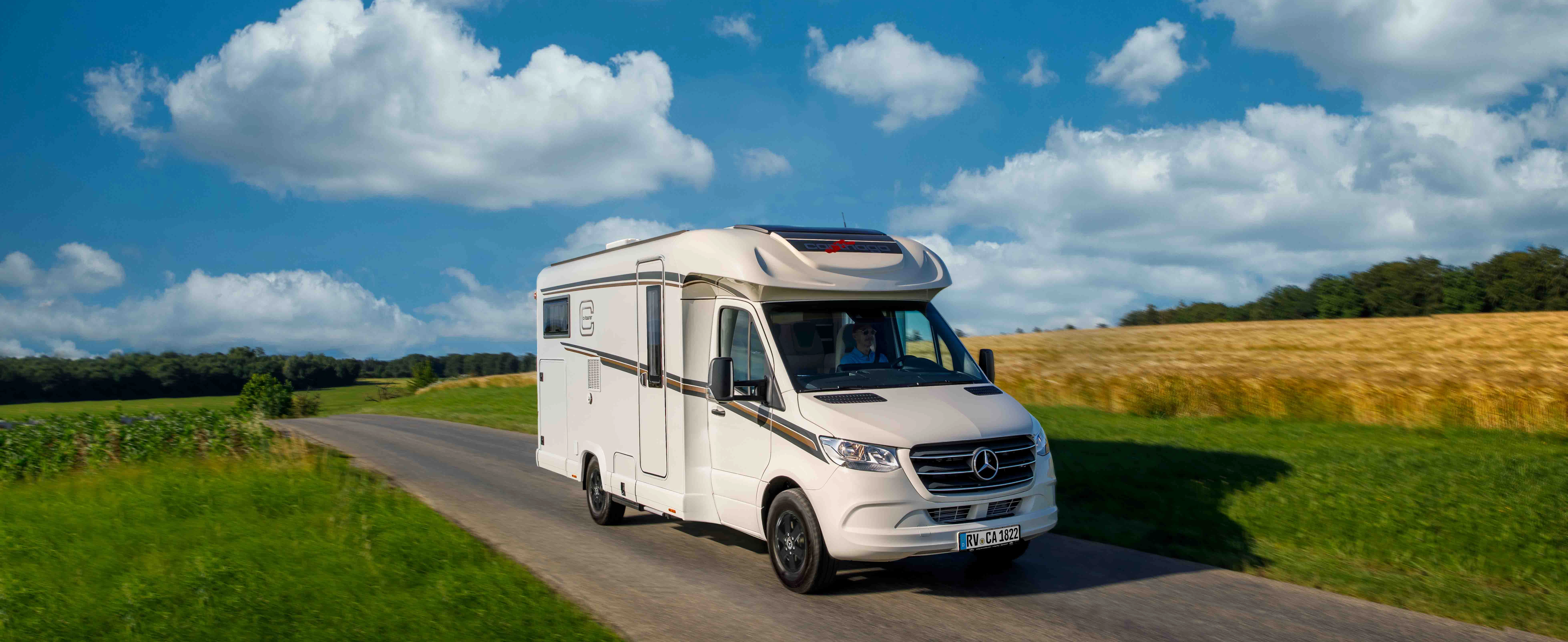 weißer, teilintegrierter Carthago auf einer Landstraße mit Feldern und blauem Himmel, Weitwinkelaufnahme
