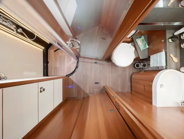 Modernes Wohnmobil-Badezimmer im Carthago Liner for Two mit Holzverkleidung, einer Dusche mit Glastür, einer runden weißen Toilette und einem weißen Waschbecken. Der Eitelkeitsbereich umfasst einen Spiegel, einen Wasserhahn und ordentlich angeordnete Toilettenartikel auf dem Tresen.