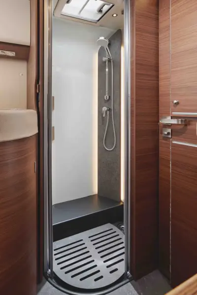 Eine kompakte Duschkabine mit Handbrause, weiße Wände, dunkle Fußböden und eine holzgetäfelte Umgebung - dieses moderne Wohnmobil-Badezimmer spiegelt den raffinierten Stil des Carthago Chic C-Line wider.