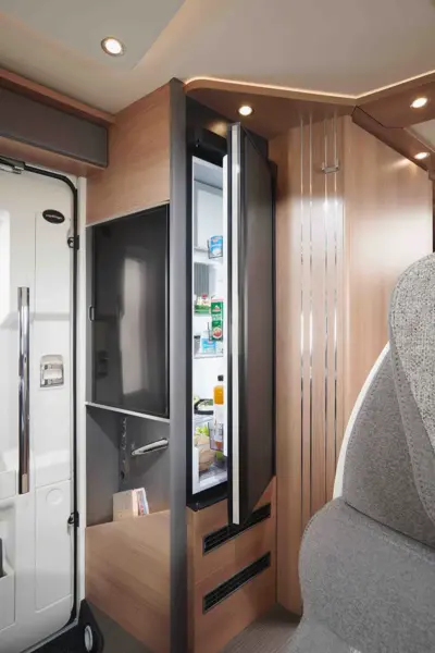 Ein modernes Carthago C Tourer Teilintegriertes Wohnmobil mit einem offenen Kühlschrank, der mit Lebensmitteln und Getränken gefüllt ist, umgeben von hellen Holzverkleidungen und eleganten, modernen Oberflächen.
