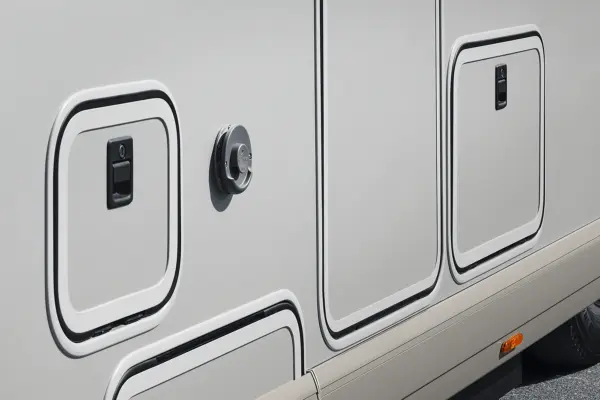 Nahaufnahme einer Seitenwand des Wohnmobils Carthago Chic C Line T. Zu sehen sind mehrere Abteiltüren, ein runder Versorgungsanschluss und ein kleiner orangefarbener Reflektor am unteren Rand.