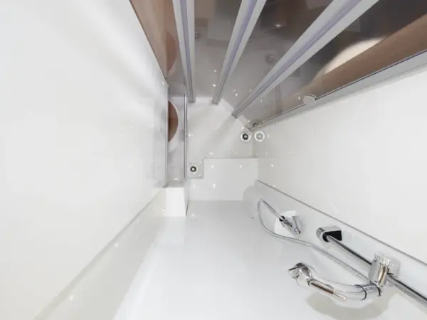 Blick von oben auf eine moderne, weiße Badewanne mit aufgesetzter Handbrause und Wasserhahn, die an das klare Design des Carthago C2-Tourer erinnert. Die Wanne ist minimalistisch, mit Glaspaneelen, die eine Seite teilweise umschließen.