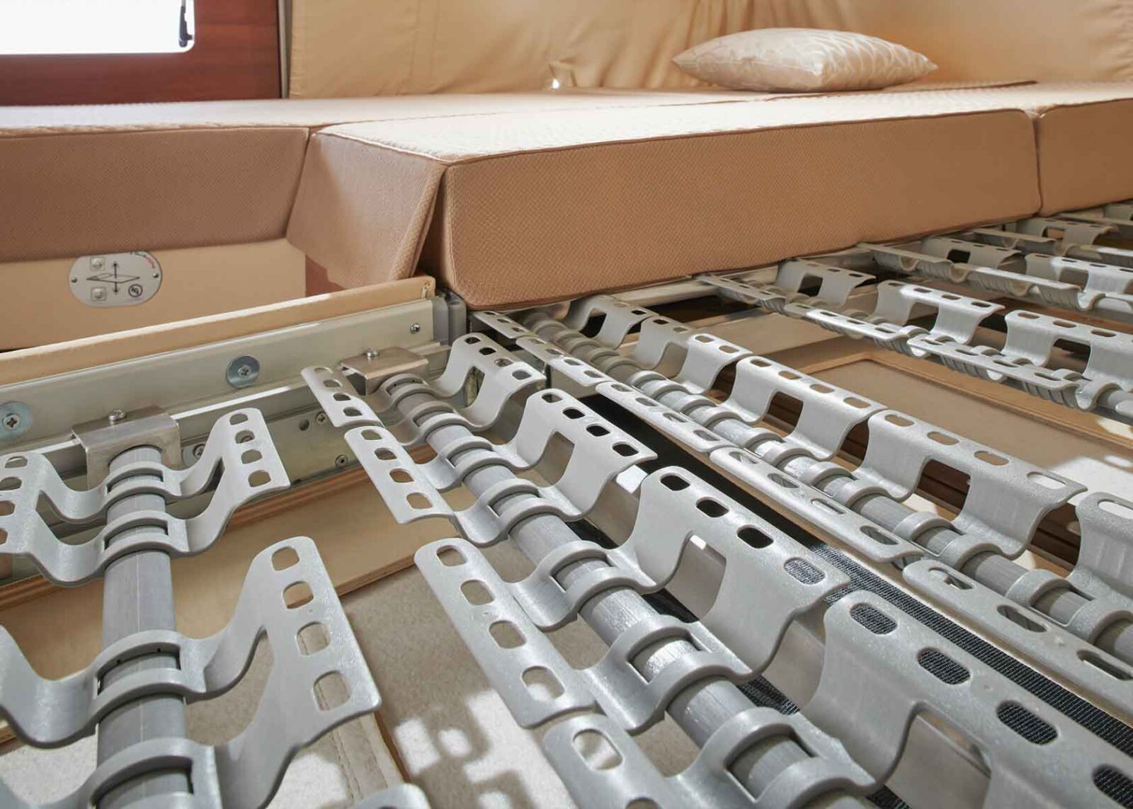 Nahaufnahme eines Metall-Lattenrosts mit flexiblen Stützen unter einer hellbraunen Matratze und einem Kissen, in einem Wohnmobil, die die strukturellen Details des Bettes zeigen.