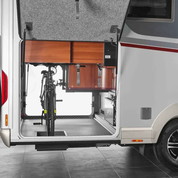 Ein hinterer Stauraum eines Carthago Liner for Two Wohnmobils mit geöffneter Tür, die ein aufrecht stehendes Fahrrad und hölzerne Ablagefächer im Inneren zeigt.
