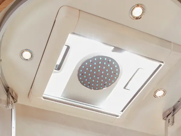 An der Decke montierte Runddusche mit blauen Sprühdüsen, umgeben von eingebauten LED-Leuchten, in einem modernen Badezimmer, das den Luxus einer Carthago Chic S Plus Einrichtung widerspiegelt.