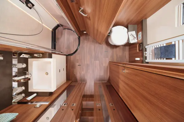 Modernes Badezimmer im Carthago Chic S Plus mit holzvertäfelten Wänden und Böden, weißem Waschbecken, Glasdusche, Toilette und mehreren Schränken und Schubladen, die von oben betrachtet ein geräumiges, organisiertes Erscheinungsbild ergeben.