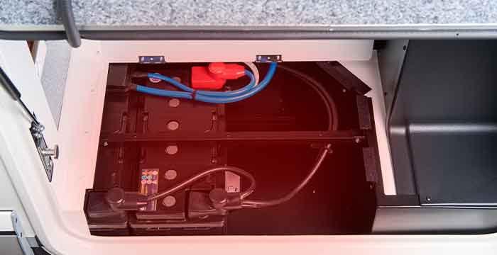 Due batterie nere sono installate in un vano al quale sono collegati cavi elettrici blu e rossi. Il vano ha una cornice bianca e un piano di lavoro grigio al di sopra.