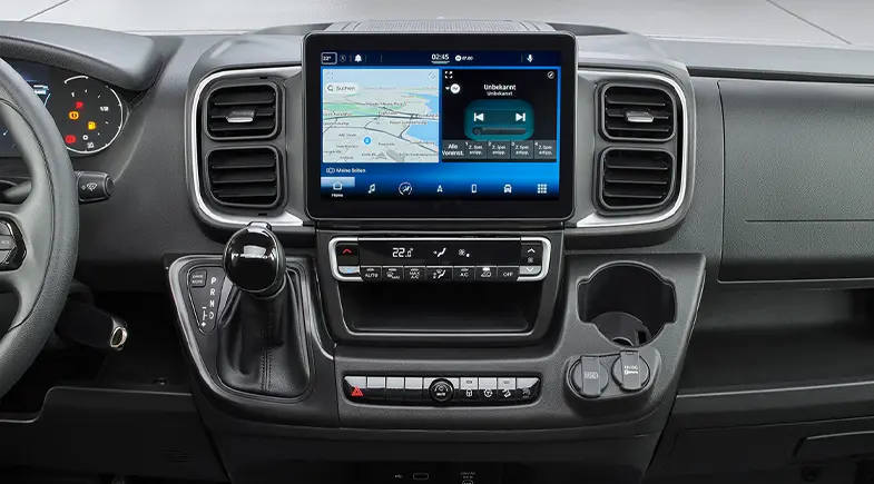 Instrumentbräda i en modern Fiat Ducato-husbil med en stor pekskärm med navigerings- och mediastyrning, kopplingsspak vänster, klimatknappar undertill och mugghållare till höger.