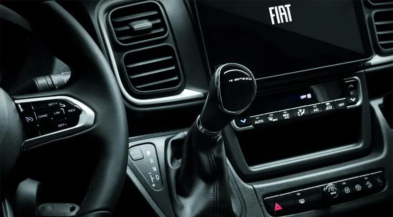 Närbild inuti en Fiat Ducato-husbil med ratt, automatväxel med 6 växlar, ventilationsmunstycken, reglage på instrumentbrädan och en bildskärm med Fiat-logga.