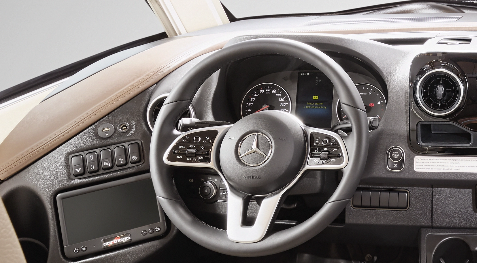 Close-up of a Mercedes-Benz steering wheel with integrated controls, dashboard gauges, infotainment display, buttons on the left-hand side and circular air vents, depicting a modern, luxurious interior.