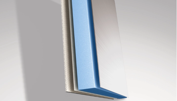 Nahaufnahme des Aufbaus einer Seitenwand mit drei sichtbaren Schichten: eine strukturierte beigefarbene Schicht, ein dicker blauer Schaumstoffkern und eine glatte, silbern glänzende Außenschicht. Das Paneel wird schräg von der Seite betrachtet.