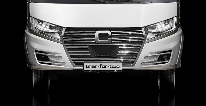 Frontansicht eines modernen weißen Wohnmobils mit eleganten Scheinwerfern, einem großen verchromten Kühlergrill und einem Nummernschild mit der Aufschrift liner-for-two vor einem schwarzen Hintergrund.