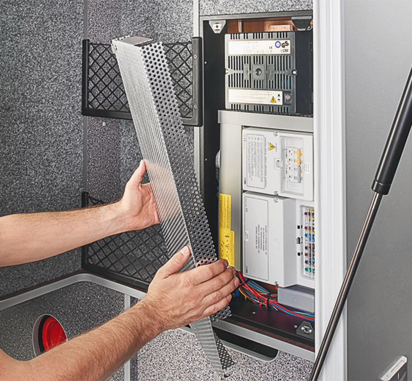 Die Hände einer Person installieren oder entfernen eine belüftete Metallabdeckung von einer elektrischen Schalttafel und geben den Blick auf Leiterplatten, Drähte und verschiedene Komponenten in einem grauen Gehäuse frei - perfekt für Schritt-für-Schritt-Anleitungen im Carthago Hilfe Portal.