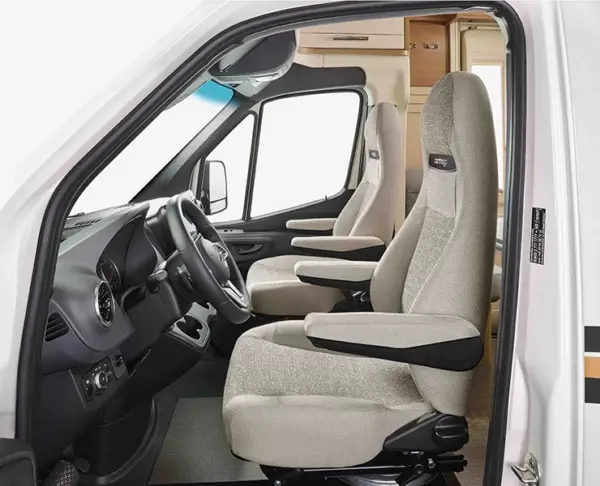 Zwei beigefarbene Vordersitze mit Armlehnen in einem modernen Wohnmobil, das den Fahrerbereich und einen Teil der Kabine mit Holzschränken im Hintergrund zeigt.