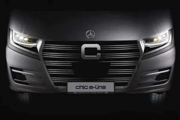Eine Nahaufnahme des Kühlergrills und der Scheinwerfer eines eleganten, modernen Fahrzeugs mit der Bezeichnung e-line, mit einem markanten C-Emblem und beleuchteten Scheinwerfern in dunkler Umgebung.