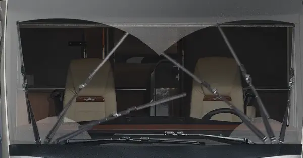 Blick durch eine regengesprenkelte Windschutzscheibe eines Fahrzeugs, in dem zwei beigefarbene Kapitänssessel zu sehen sind. Die Scheibenwischer sind in Bewegung und wischen eine herzförmige Fläche auf dem Glas frei.