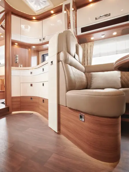 Luxuriöses Wohnmobil-Interieur mit hellbraunen Ledersitzen, cremefarbenen und holzgetäfelten Schränken, Holzfußböden und warmer Deckenbeleuchtung für eine moderne, gemütliche Atmosphäre.