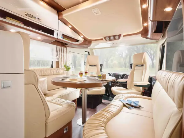 Luxuriöses Carthago Chic S Plus Wohnmobil-Interieur mit cremefarbenen Ledersitzen, einem runden Esstisch für das Frühstück und großen Fenstern, die natürliches Licht hereinlassen. Der Raum wirkt modern und komfortabel.