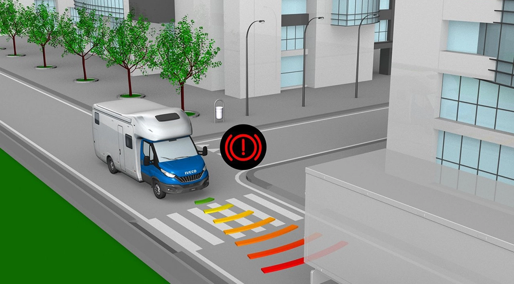 A blue and white Iveco Daily motorhome approaching a zebra crossing on an urban street. Coloured lines and a brake warning symbol indicate that the vehicle’s automatic Advanced Emergency Braking System has detected an obstacle in front of it.