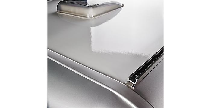 Primo piano del tetto liscio e metallico di un veicolo, con un elemento rettangolare in rilievo con bordi arrotondati e una superficie lucida. L’immagine mette in risalto le linee pulite e la superficie riflettente.