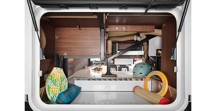 View into the storage space in a motorhome, containing a pair of paddles, a helmet, a foam roll and a ring toy, with shelves and pipes in the background.