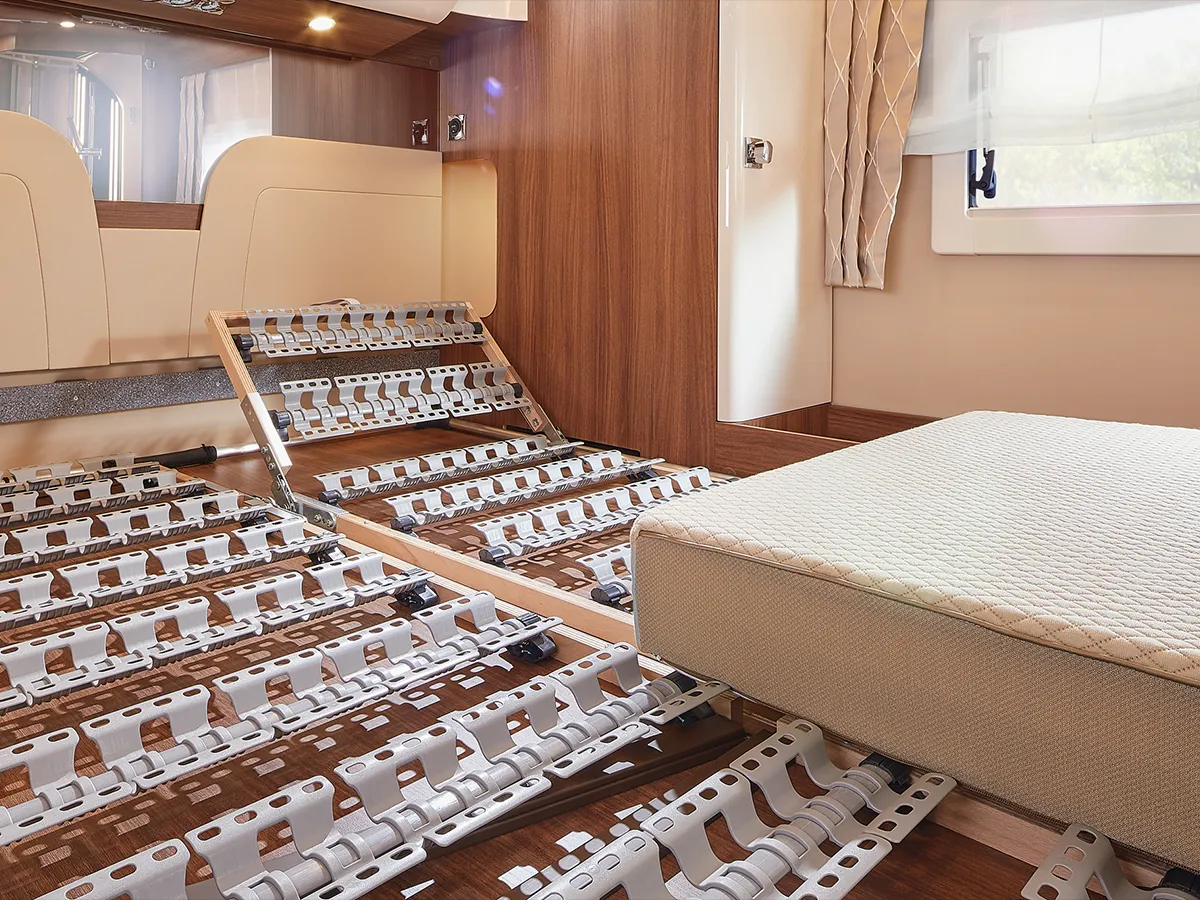 Ein modernes Schlafzimmer mit einem verstellbaren Lattenrost, teilweise erhöht, neben einer Matratze, die an den erstklassigen Komfort eines Carthago Chic E-Line erinnert. Der Raum ist mit Holzvertäfelung, hellen Wänden und einem großen Fenster mit Vorhängen ausgestattet.