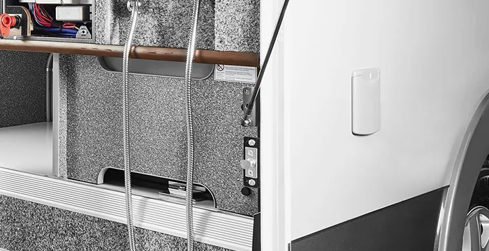 Nahaufnahme des Außenstauraums eines Carthago Chic E-Line Wohnmobils mit einer eingebauten Dusche mit zwei Schläuchen, Schaltern und Regalen mit verschiedenen Geräten.