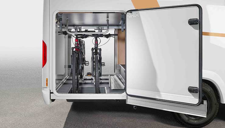 An open storage compartment in the rear of a white motorhome, where two bikes are securely attached. The door is open, revealing the neat and tidy interior and bike carrier system.