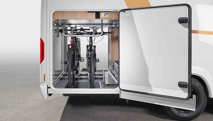 The image shows the open rear storage compartment of a motorhome with two bikes securely attached to a carrier. The storage space door is open, revealing the tidy interior.