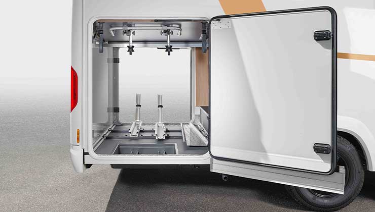 Close-up of an open storage compartment on the side of a motorhome, with bicycle racks and carriers attached.