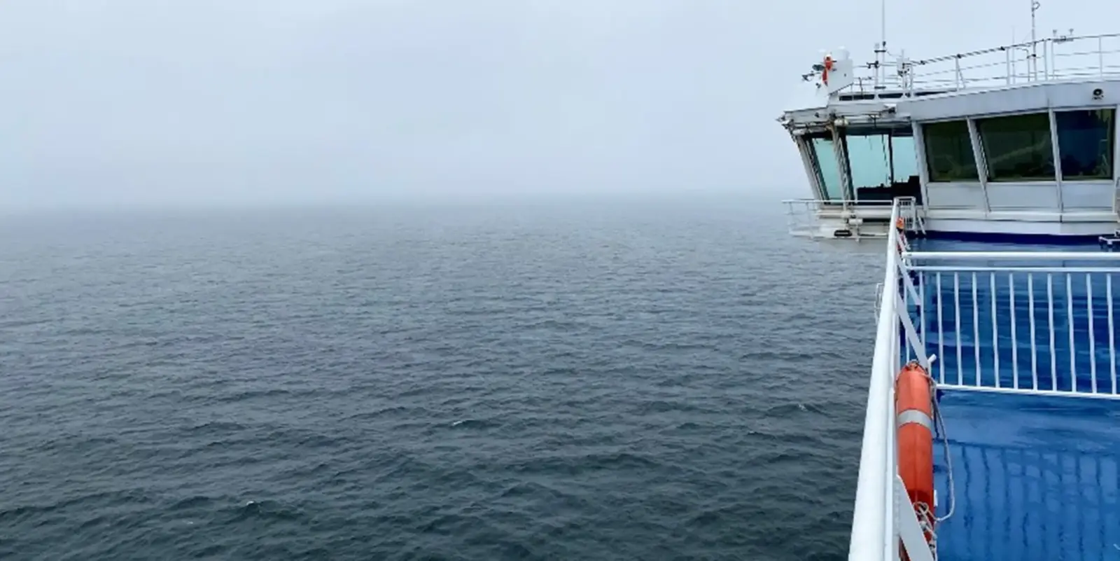A view of the open ocean under a grey, overcast sky, with the bridge of a ship stretching across the water from the right side of the painting.