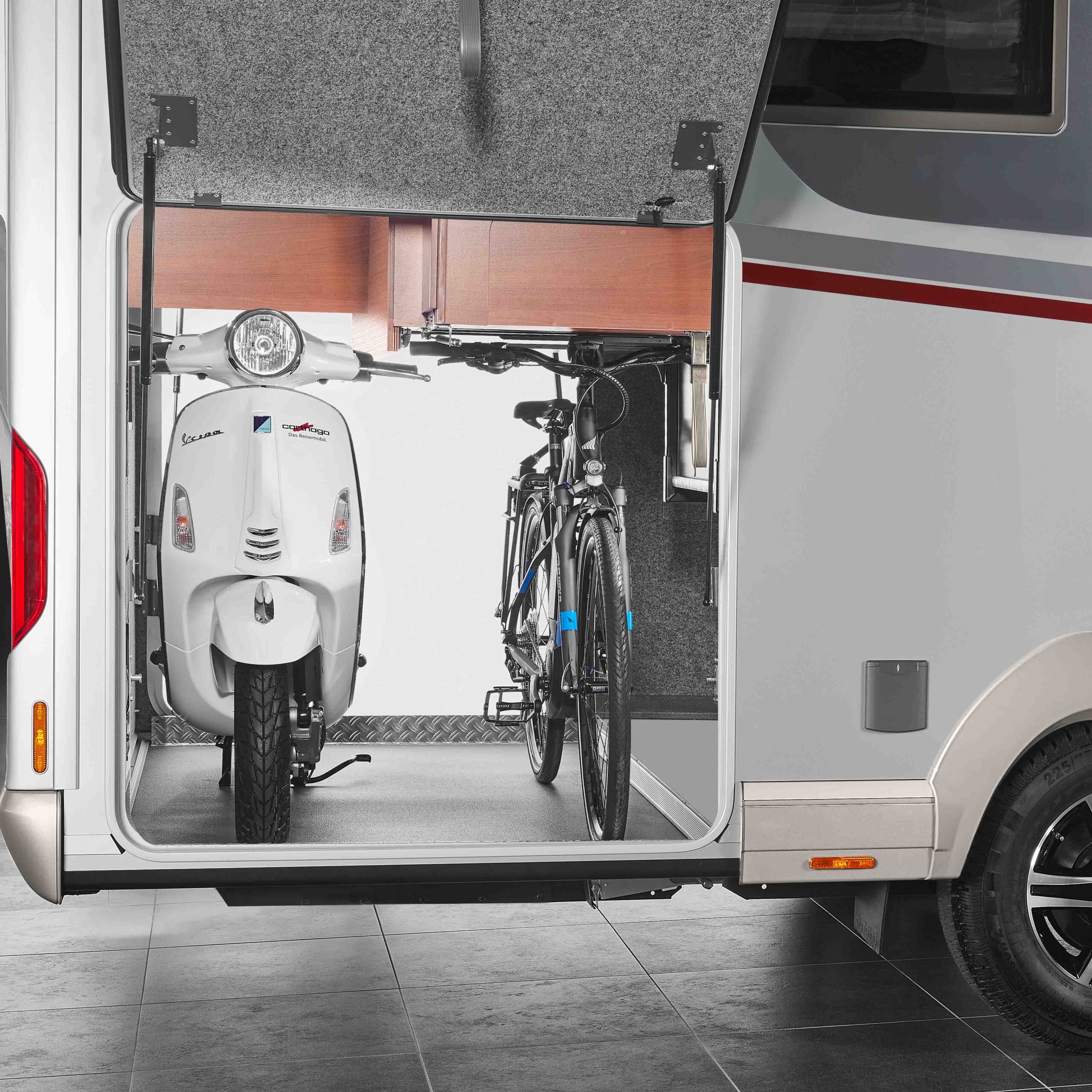 Ein Roller und ein Fahrrad sind sicher im hinteren Staufach eines Carthago Liner for Two Reisemobils geparkt. Die Tür des Staufachs ist geöffnet und der organisierte Innenraum ist bereit für den Transport.