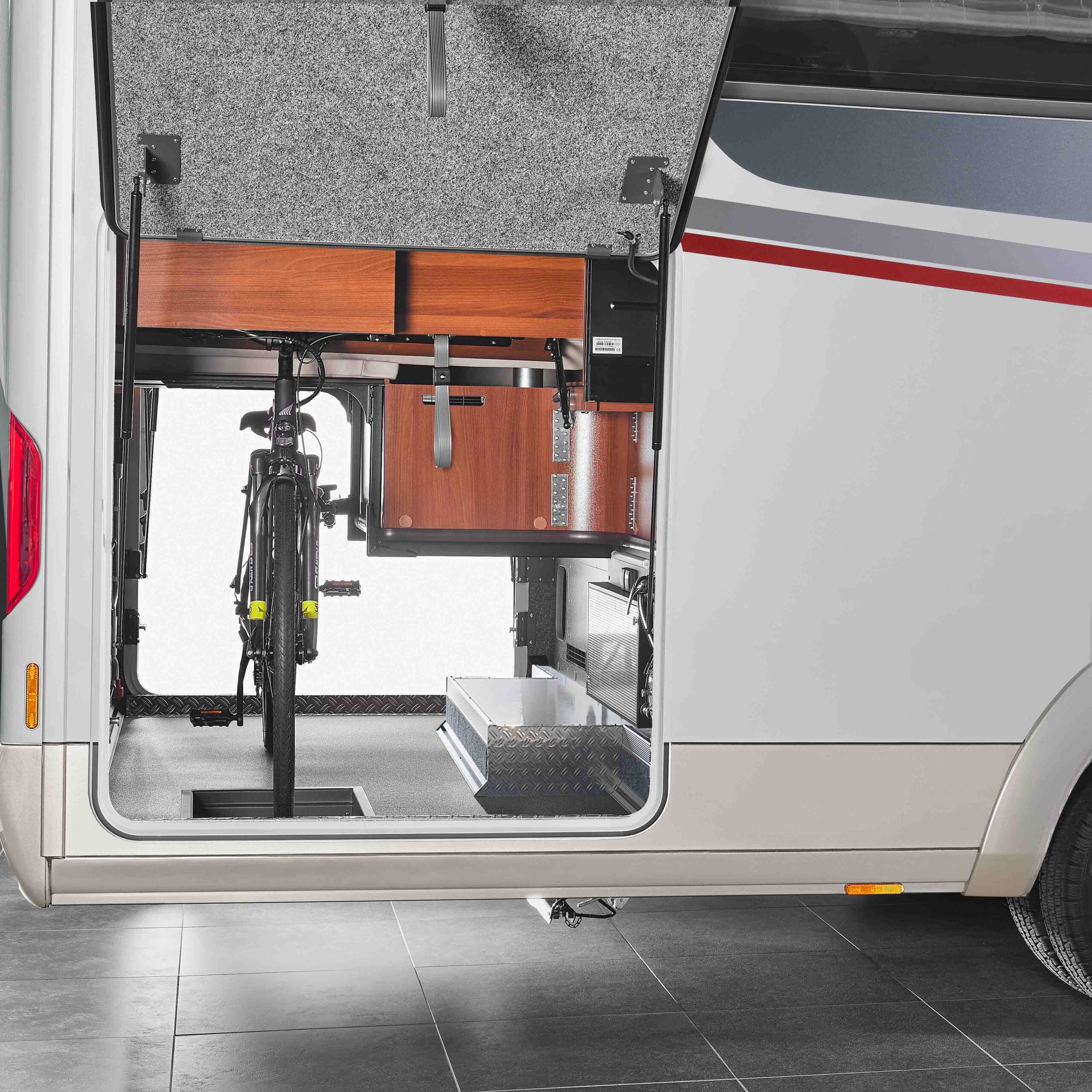 Ansicht eines Carthago Liner for Two Wohnmobil-Stauraums mit geöffneter Tür. Zu sehen sind ein fest montiertes Fahrrad, Holzregale und verschiedene Stauschubladen und -fächer im Inneren.