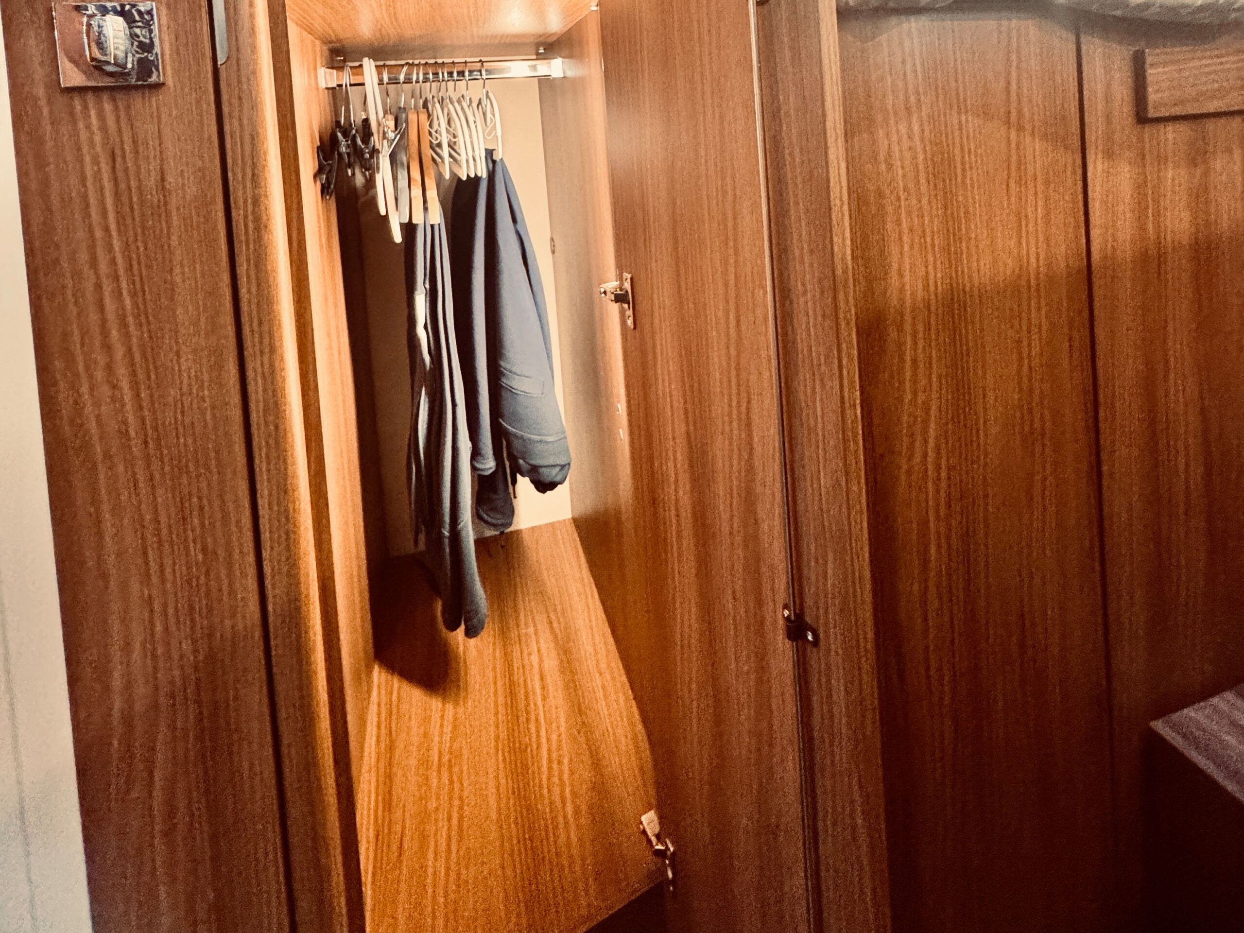 Una credenza in legno a vista con diverse grucce vuote e alcune giacche scure richiama alla mente gli interni accoglienti spesso descritti nei resoconti di viaggio sulla Finlandia, effecto accentuato da un'illuminazione calda e da una porta socchiusa.