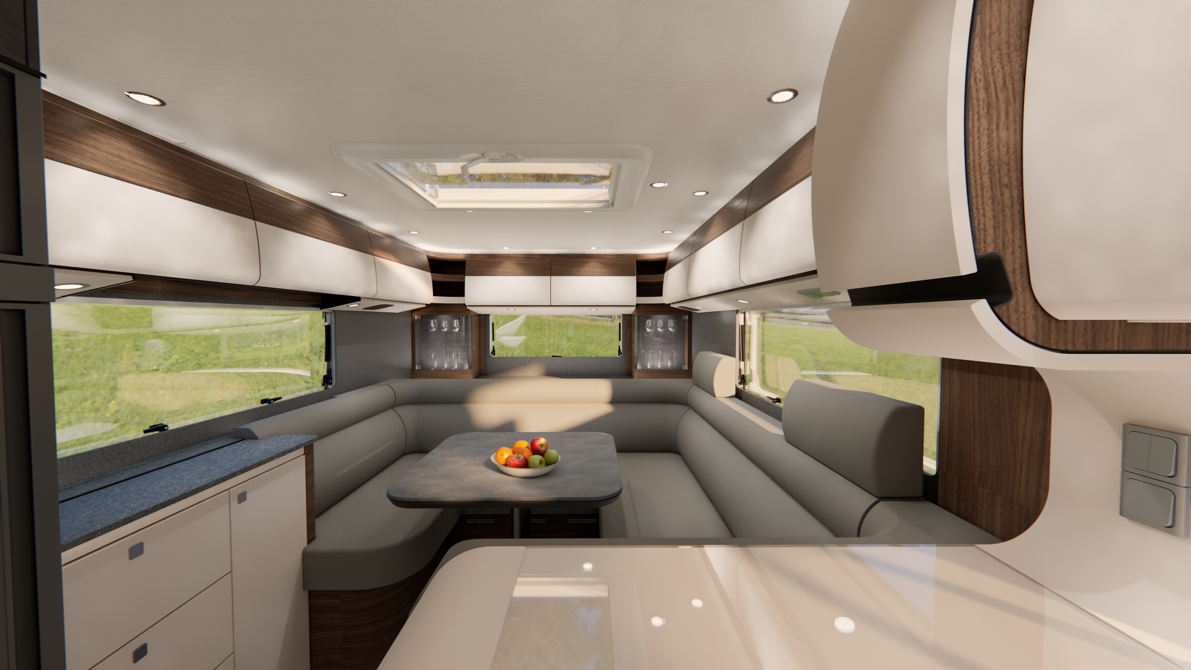 Ein modernes Wohnmobil-Interieur mit geschwungenen beigen Sitzgelegenheiten, einem dunklen Tisch mit einer Obstschale, Holzakzenten, großen Fenstern, Hängeschränken und Deckenleuchten, das einen hellen, gemütlichen Ess- und Wohnbereich mit malerischem Ausblick nach draußen schafft.