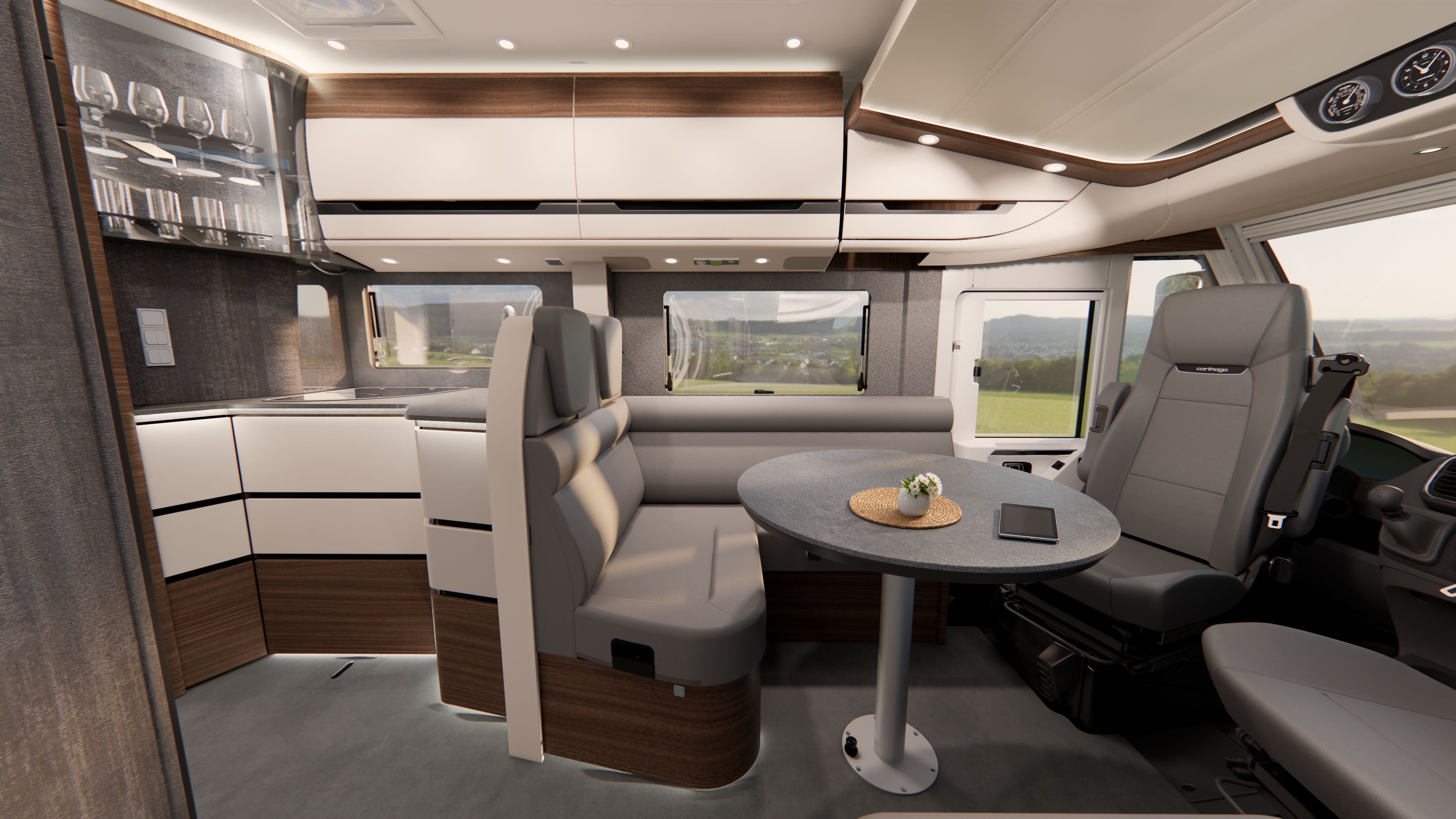 Moderne Wohnmobil-Innenausstattung mit Essbereich, rundem Tisch, eingebauten Sitzbänken, einem Fahrersitz und Küchenschränken. Durch die Fenster bietet sich ein malerischer Ausblick auf die Landschaft. Auf dem Tisch liegen ein Smartphone und eine kleine Pflanze.