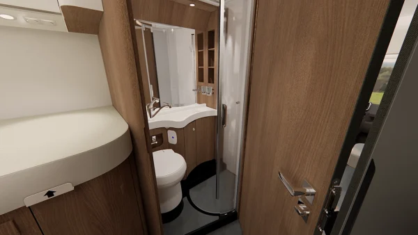 Das kompakte Badezimmer des Carthago C2-Tourer verfügt über eine elegante Holzvertäfelung, eine Toilette, ein kleines Waschbecken mit Spiegel sowie eine abgerundete Dusche mit Glastür. Auf der linken Seite ist ein Bett teilweise zu sehen.