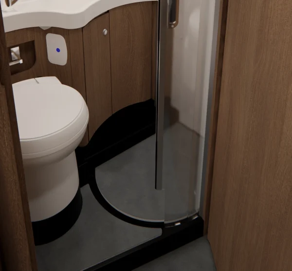 Das kleine Badezimmer im Carthago C2-Tourer verfügt über eine weiße Toilette, holzvertäfelte Wände, eine Duschkabinentür aus gebogenem Glas und einen grauen Boden. In der Ecke sind Teile eines weißen Waschbeckens und einer Arbeitsplatte zu sehen.