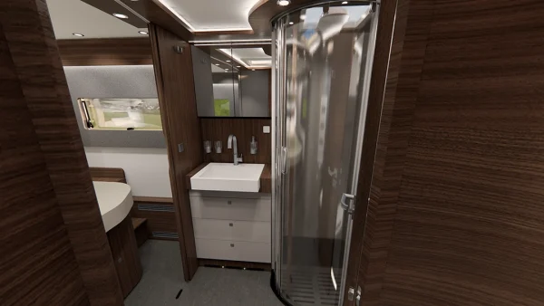 Modernes Wohnmobil-Badezimmer im Carthago Chic E Line mit eleganter Holzvertäfelung, einer runden Dusche mit Glastür, weißem Waschbecken und Waschtischplatte, Schubladen darunter, einem Spiegel darüber sowie stimmungsvoller Beleuchtung. Im Hintergrund ist ein Bett mit Fenster zu sehen.