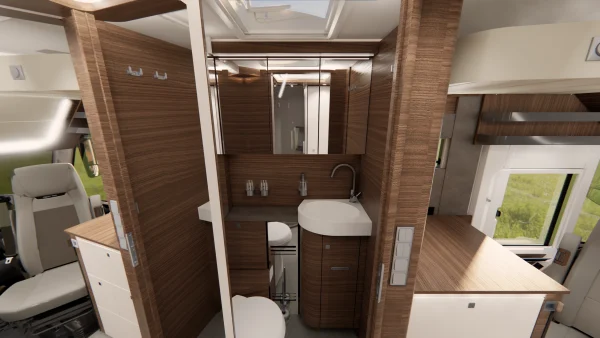 Modernes Wohnmobil-Badezimmer mit Holzvertäfelung, einem geschwungenen Waschbecken, Spiegel, Toilette, Stauschränken und integrierter Beleuchtung – charakteristische Merkmale des Carthago Liner-for-Two. Auf beiden Seiten sind Teile des Fahrersitzes und des Küchenbereichs zu sehen.