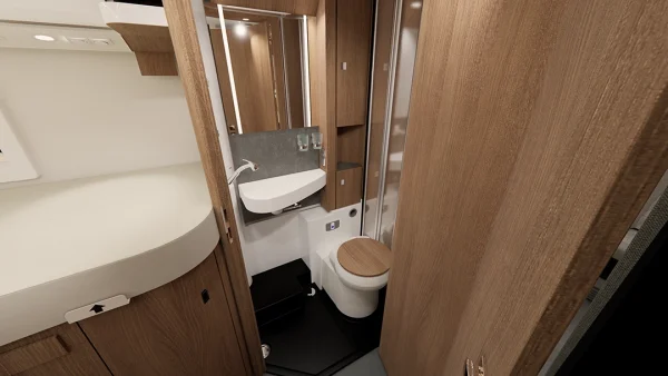 Kompaktes Badezimmer im Carthago C2-Tourer mit holzvertäfelten Wänden, einem kleinen weißen Waschbecken, einem Spiegel darüber und einer Toilette mit Holzdeckel. Zu sehen sind Regale und Stauschränke, die alle so gestaltet sind, dass sie den begrenzten Platz im C2-Tourer effizient ausnutzen.
