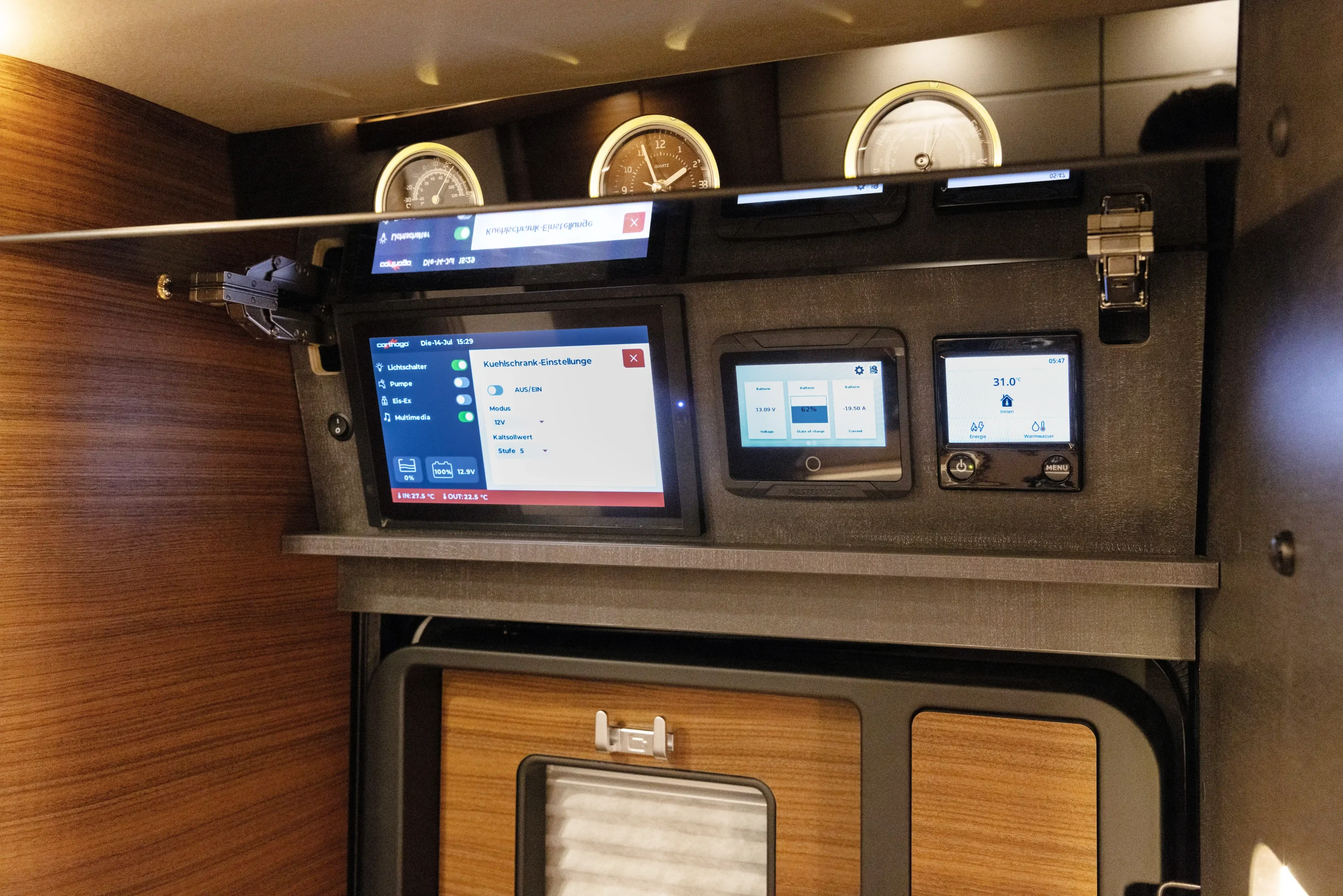 Bedienfeld mit mehreren digitalen Anzeigen, Messgeräten und Schaltern, eingebettet in einen dunklen Rahmen, der von Holzverkleidungen umgeben ist, möglicherweise im Inneren eines Carthago Liner for Two oder eines modernen Geräteraums.