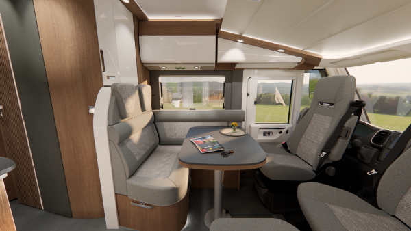 Moderne Wohnmobil-Innenausstattung mit grauen Polstersitzen, einem gedeckten Tisch mit Tasse, Teller und Blumen sowie Zeitschriften und Schlüsseln. Große Fenster bieten einen Blick auf einen begrünten Außenbereich und schaffen so eine einladende Atmosphäre in diesem Carthago C2-Tourer.