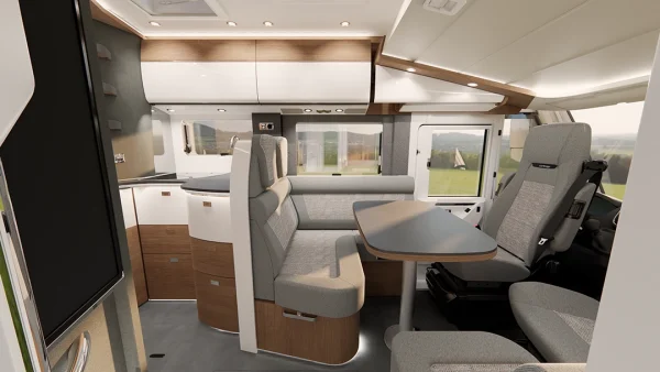 Moderner Wohnmobil-Innenraum mit einer kompakten Küche, einem Esstisch mit gepolsterten Sitzbänken, Drehstühlen und großen Fenstern, durch die man das Tageslicht draußen sehen kann. Das Design besticht durch helle Holz- und weiße Oberflächen, die den eleganten Stil des Carthago C2-Tourer widerspiegeln.