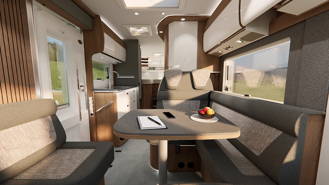 Moderne Wohnmobil-Innenausstattung mit grauen Polstersitzgelegenheiten rund um einen Tisch in diesem atemberaubenden Carthago C2-Tourer. Auf dem Tisch stehen eine Obstschale, ein Notizbuch und ein Handy. In dem hellen, aufgeräumten Raum sind der Küchenbereich, Schränke, Fenster und Akzente aus hellem Holz zu sehen.