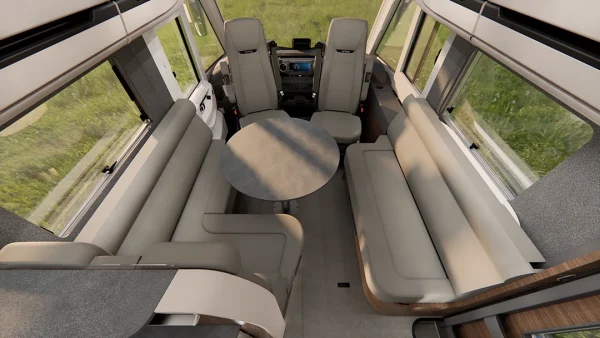 Innenraum eines Wohnmobils der Carthago Chic E-Line mit zwei langen beigen Sofas, einem runden Tisch in der Mitte, großen Fenstern und dem vorne sichtbaren Fahrerbereich.