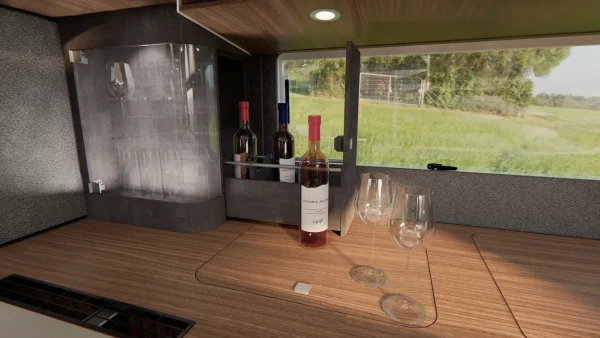Drei Weinflaschen in einem offenen Schrank, eine Flasche auf der Holztheke und drei leere Weingläser stehen daneben – das perfekte Ambiente für einen entspannten Abend im Carthago Liner for Two. Ein Fenster hinter ihnen gibt den Blick auf eine grasbewachsene Landschaft frei und trägt so zur einladenden Atmosphäre bei.