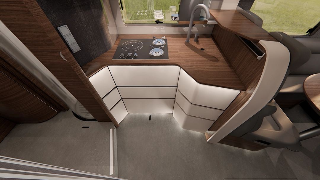 Moderne Wohnmobilküche mit Holz- und weißen Schränken, einem kleinen Kochfeld mit zwei Kochstellen, einer Spüle und einer geschwungenen Arbeitsplatte. Durch die nahegelegenen Fenster fällt Tageslicht herein und erhellt den Raum – ein Spiegelbild des hochwertigen Designs der Carthago Chic E-Linie.
